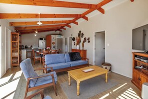 A spacious living area with a sofa, chairs, a coffee table, and a television. A kitchen is visible in the background.