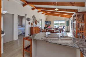 A spacious living area with a large wooden ceiling, a dining table set for four, and a television mounted on the wall. - The Hideaway - Omaha Holiday Home (Omaha)