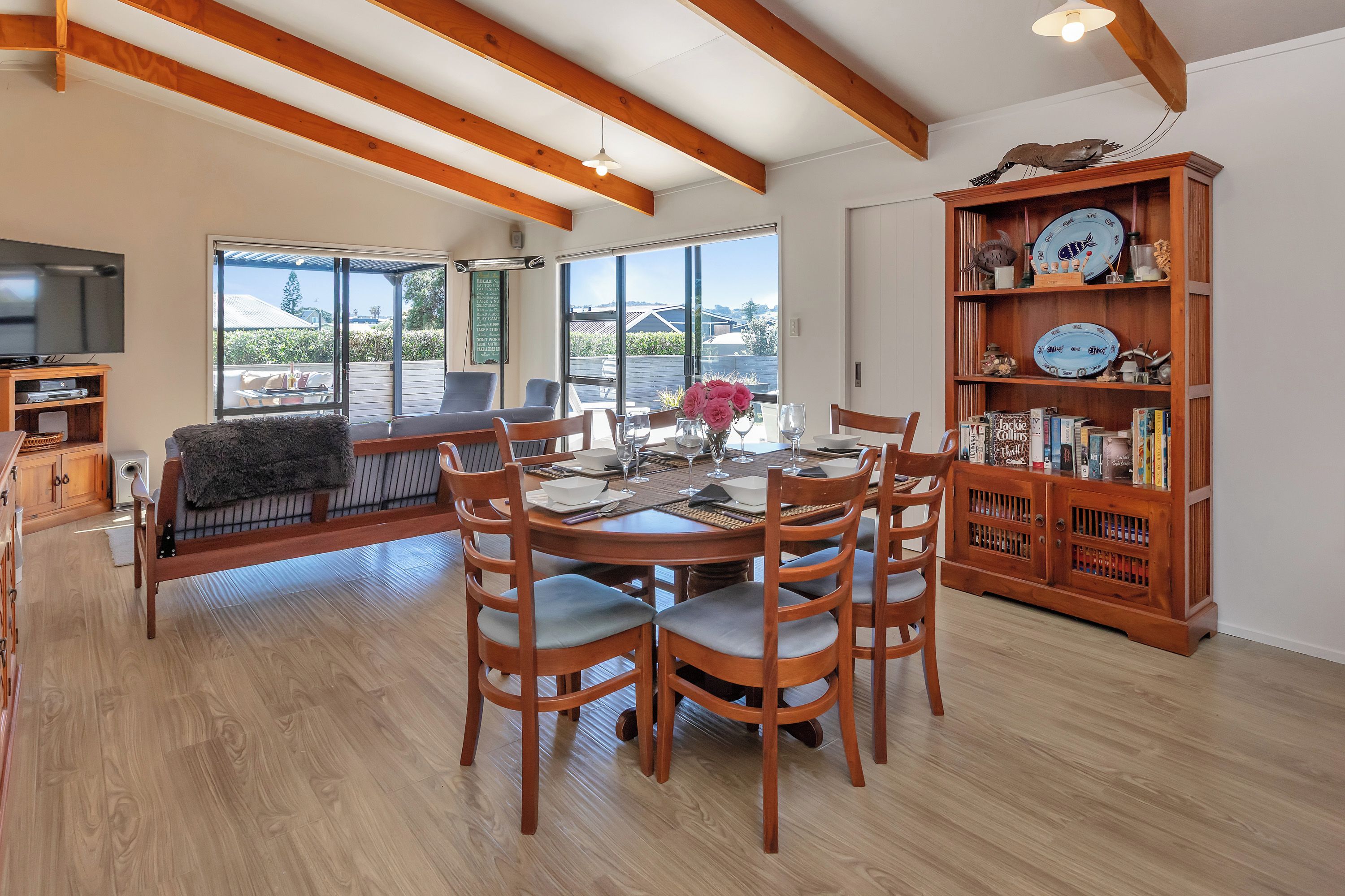 A dining area with a wooden table and chairs, a bookshelf with decorative plates, and a television in the background.
