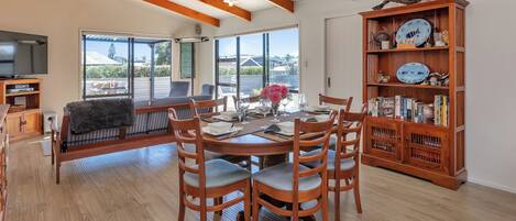 A dining area with a wooden table and chairs, a bookshelf with decorative plates, and a television in the background.
