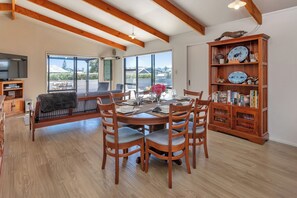 A dining area with a wooden table and chairs, a bookshelf with decorative plates, and a television in the background. - The Hideaway - Omaha Holiday Home (Omaha)