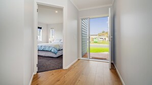 A hallway leading to a bedroom with a bed and a view of the outdoors. - Seascape - Cooks Beach Holiday Home (Cooks Beach)
