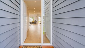 A modern house with a sliding glass door leading to a spacious interior with a kitchen and living area. - Seascape - Cooks Beach Holiday Home (Cooks Beach)