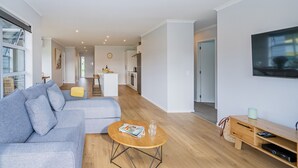 A modern living room with a grey sectional sofa, a wooden coffee table, and a TV mounted on the wall. - Seascape - Cooks Beach Holiday Home (Cooks Beach)