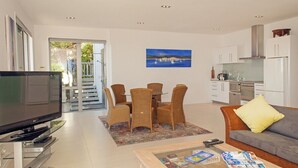 A modern living room with a flat-screen TV, wicker furniture, a sofa with a yellow pillow, and a painting on the wall. - The Ridge at Tairua - Tairua Apartment (Tairua)