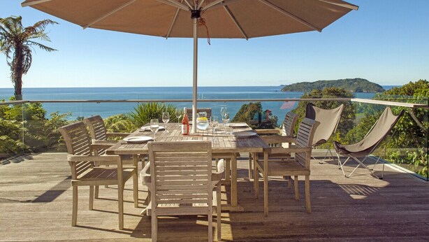 A wooden deck with a table and chairs, an umbrella, and a view of the ocean. - The Ridge at Tairua - Tairua Apartment (Tairua)