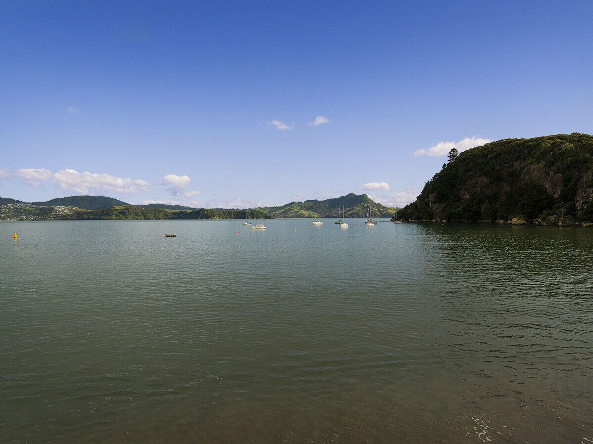 A calm lake with several boats anchored, surrounded by hills and a clear sky.