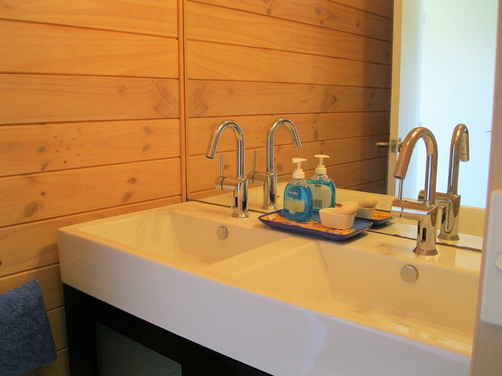 A bathroom with a double sink, wooden panel walls, and two bottles of hand soap on the sink.