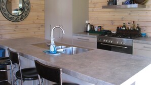 A modern kitchen with a central island, stainless steel sink, and a gas stove. - Paradise in Flaxmill Bay - Flaxmill Bay Home (Cooks Beach)
