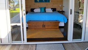 A bedroom with a bed, a wooden chest, and a view of the outdoors. - Paradise in Flaxmill Bay - Flaxmill Bay Home (Cooks Beach)