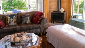 A cozy living room with a sofa, a glass coffee table with decorative items, a fireplace, and a view of greenery outside. - Paradise in Flaxmill Bay - Flaxmill Bay Home (Cooks Beach)