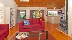 A spacious living room with a red sofa, a glass coffee table, and a wooden ceiling. - Carefree at Cooks - Cooks Beach Bach (Cooks Beach)
