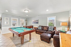 A pool table in a living room with a sofa and ottoman.