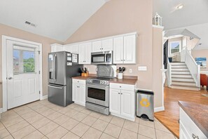 A kitchen with white cabinets, stainless steel appliances, and a trash can with a recycling symbol.