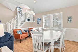 A dining area with a white table and chairs, a staircase with white railings, and a bookshelf.