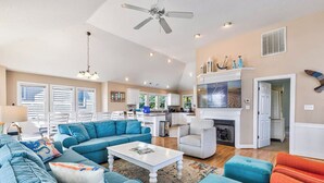A spacious living room with a large sofa, a coffee table, and a fireplace. There is a kitchen in the background with a dining area. - Ocean Paradise | 670 ft from the Beach | Private Pool, Hot Tub | Corolla (Corolla)