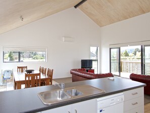 A modern kitchen with a built-in dishwasher, a dining area with wooden chairs, and a red leather sofa.