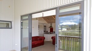 Um interior moderno com uma porta de vidro deslizante que dá para uma varanda, um sofá de couro vermelho e uma cozinha visível através da porta.