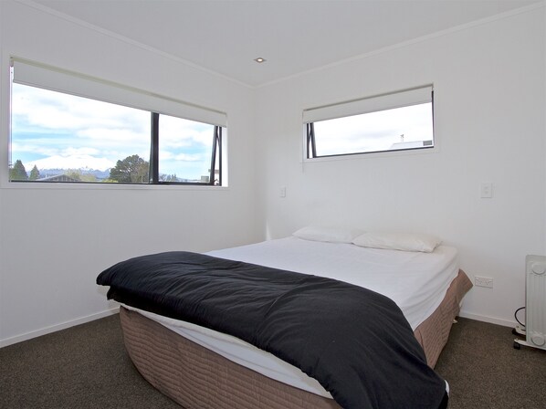 A bedroom with a bed, two windows, and a radiator.