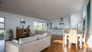 Ein geräumiger Wohnbereich mit einer Couch, einem Esstisch und Stühlen, einer Küche im Hintergrund und großen Fenstern.