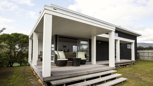 Ein modernes Haus mit überdachter Veranda, Sitzgelegenheiten im Freien und Blick auf die umliegende Landschaft.
