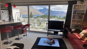 A living room with a large window, a TV, red chairs, a sofa, and a bookshelf. - Rooftop garden, Lakeview, 5 mins walk to town (Queenstown Hill)