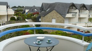 Un balcón con una mesa redonda y dos sillas, con vista a una zona residencial de edificios de piedra y al mar.