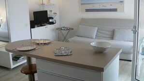 Una habitación moderna y luminosa con comedor, sofá y un cuadro de una playa.