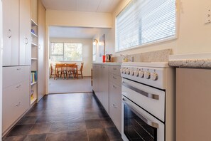 Une cuisine équipée d’une cuisinière, d’un four et de placards, qui donne sur un coin repas avec une table et des chaises.