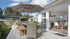 An outdoor patio with a wooden deck, wicker furniture, and a large umbrella.