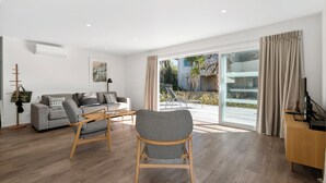 A modern living room with a grey sofa, a patterned chair, a wooden coffee table, and a TV stand.