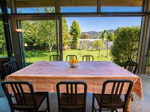 Un patio techado con una mesa dispuesta para dos personas, con un mantel estampado y un cuenco de naranjas.