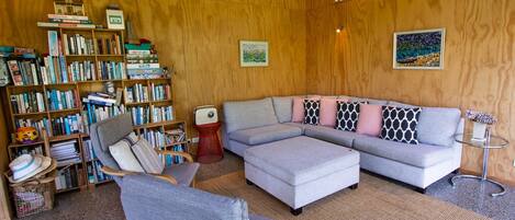 Een gezellige woonkamer met een hoekbank, een boekenplank vol boeken en een houten wand.