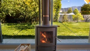 Una estufa de leña en una habitación con un ventanal grande que da a un jardín cubierto de césped.