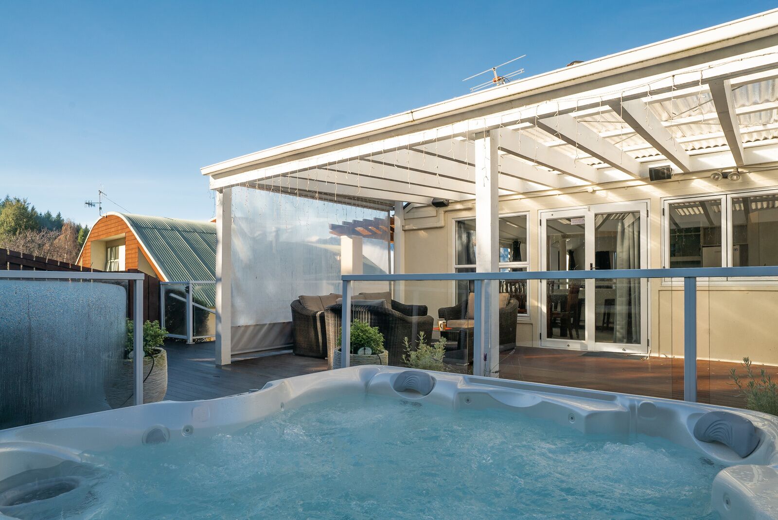 Ein Whirlpool in einer überdachten Außenanlage mit Terrasse, Sitzgelegenheiten und Blick auf ein Haus.