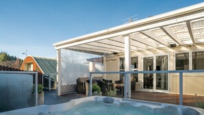 Una bañera de hidromasaje en un espacio exterior cubierto con un patio, asientos y vistas a una casa.