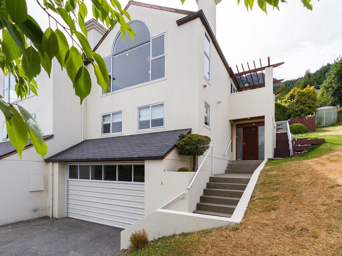 Une maison à deux étages avec un garage, un escalier menant à la porte d’entrée et un petit jardin.