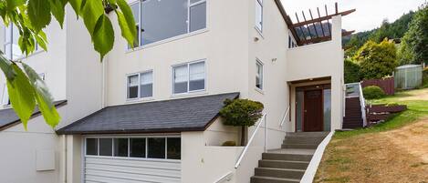 Une maison à deux étages avec un garage, un escalier menant à la porte d’entrée et un petit jardin.