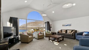 Un salón amplio con un gran ventanal que ofrece vistas a un paisaje costero, un televisor de pantalla plana y muebles modernos.