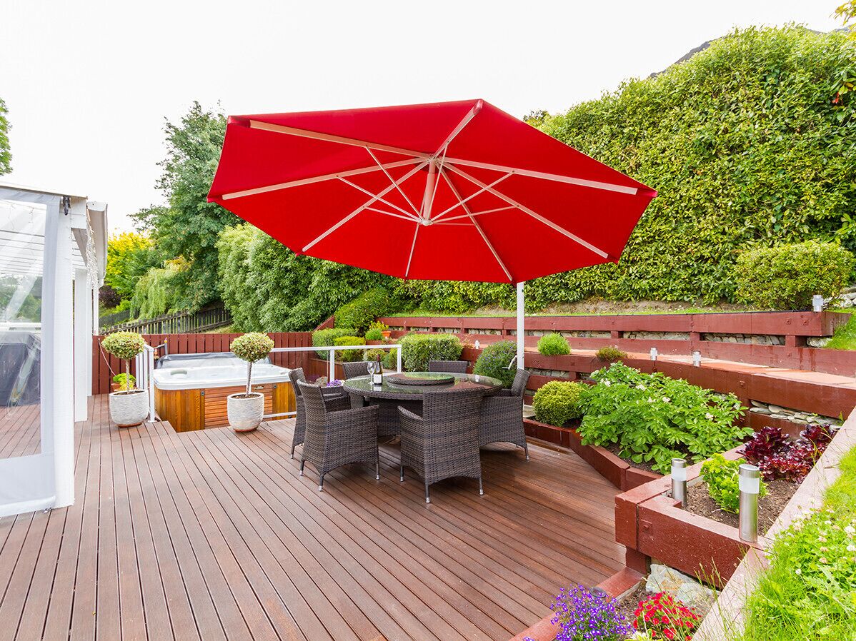 Una terraza de madera con un paraguas rojo, muebles de mimbre y un jacuzzi.