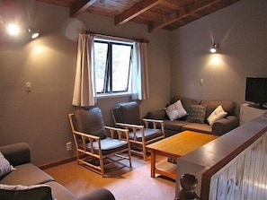 A cozy living room with a wooden ceiling, a sofa set, two rocking chairs, a coffee table, and a television.