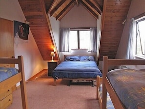 A bedroom with a sloped ceiling, a bed with blue bedding, a nightstand with a lamp, and a window with curtains.