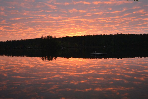 Auringonlasku tyynen järven yllä, ja etualalla näkyy vene.