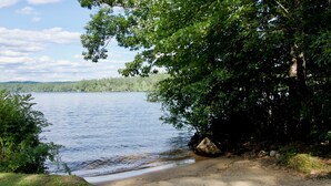 A lakeside view with a sandy beach, trees, and a clear sky.