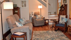 A living room with a sofa, armchairs, a coffee table, a lamp, and a staircase.