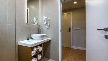 Ein modernes Badezimmer mit einem weißen Waschbecken, einem Spiegel, einem Fön und einem Holzregal mit Handtüchern.