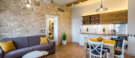 Una cocina moderna con armarios de madera, un comedor con mesa y sillas blancas, y una sala de estar con sofá y cojines amarillos.