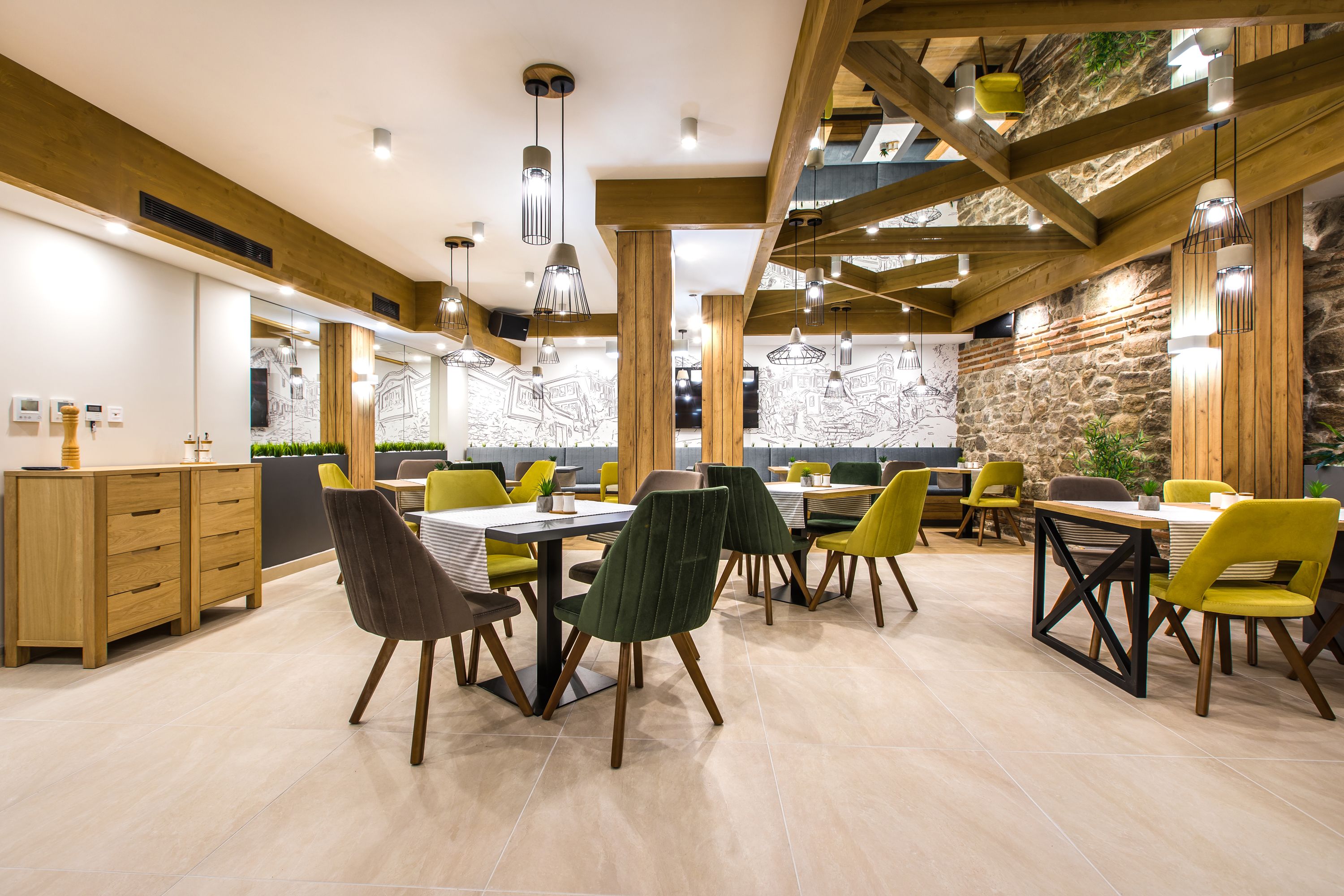 A modern dining area with wooden beams, green and yellow chairs, and a stone accent wall.