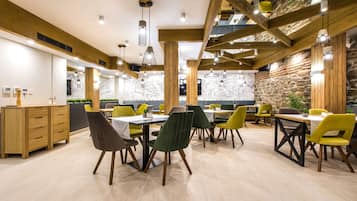 A modern dining area with wooden beams, green and yellow chairs, and a stone accent wall.