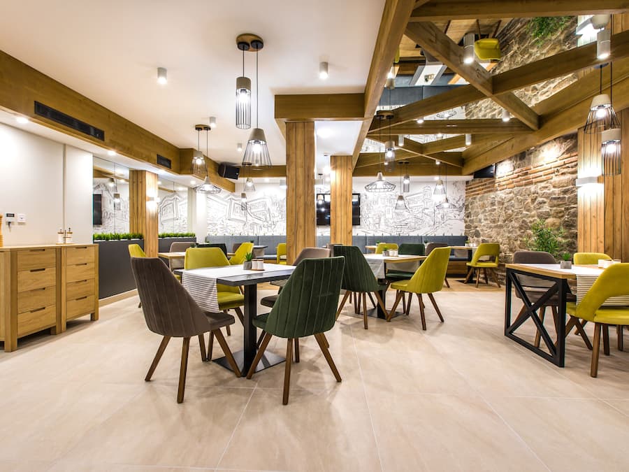A modern dining area with wooden beams, green and yellow chairs, and a stone accent wall.